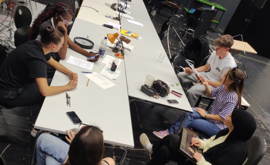 Die Schülerinnen und Schüler sitzen um einen Tisch und diskutieren.
