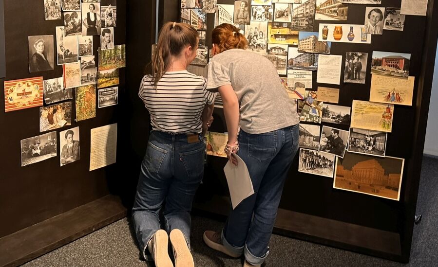 Zwei Schülerinnen stehen in der Ausstellung vor den Fotos der Familie Wels im schwarzen, großen Koffer